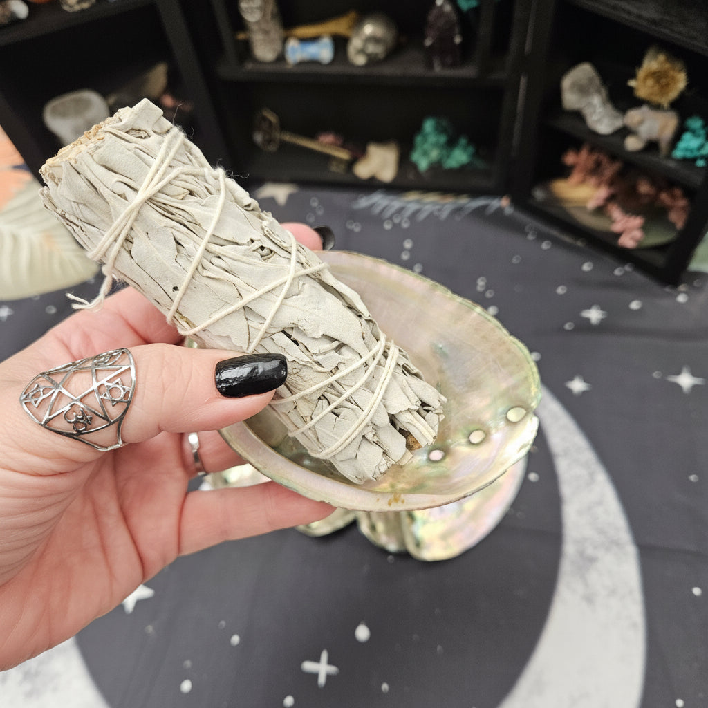 Hand holding sage smudge stick with a moon and star design in the background