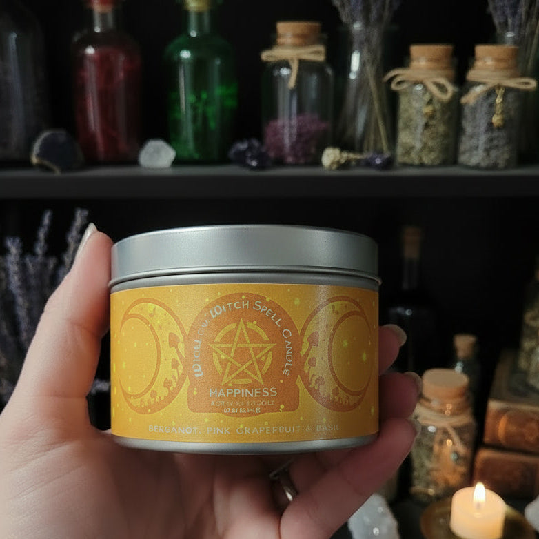 Hand holding a candle tin labeled 'Happiness' in front of an mystical shelf with bottles and candles.