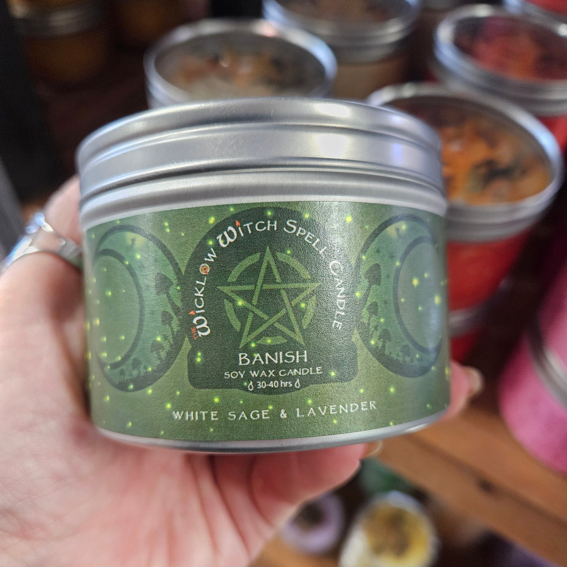 Hand holding a green candle tin with a star design, surrounded by other candles.