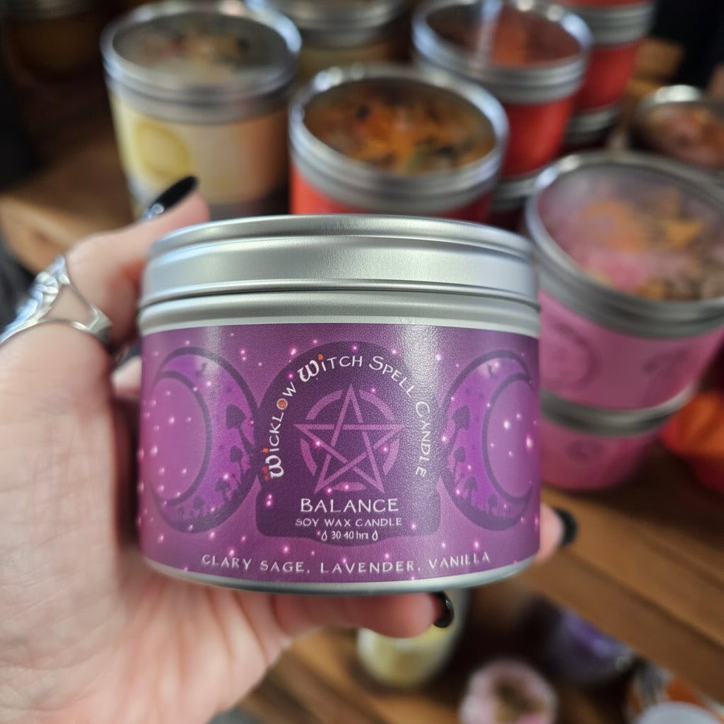 Hand holding a purple candle tin labeled 'Witch Spell Candle' with other similar candles in the background.