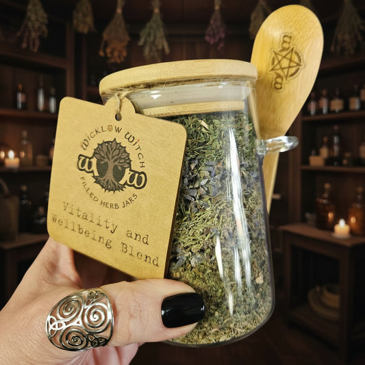 Glass jar filled with herbs labeled 'Vitality and Wellbeing Blend' held by a hand.