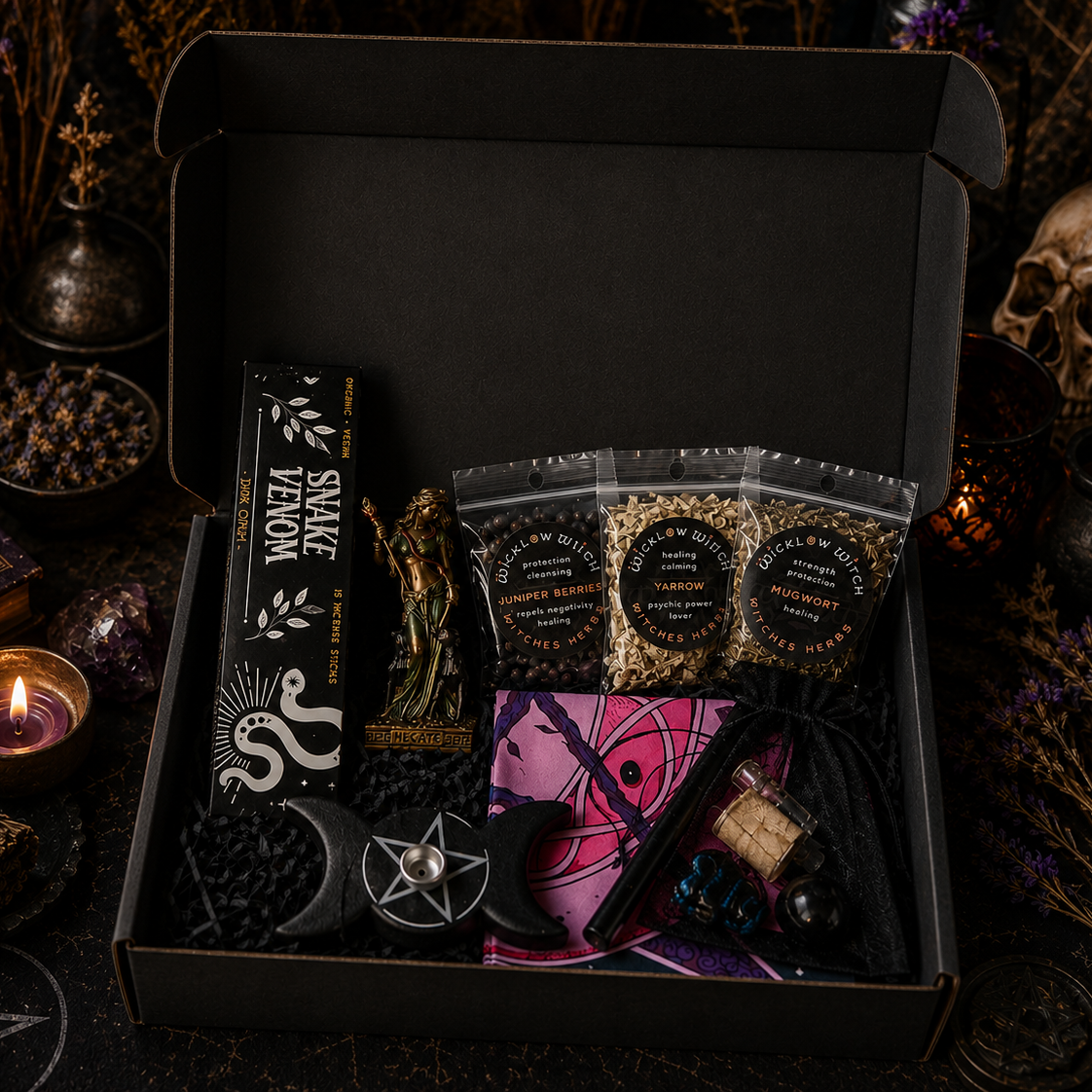 Open black box containing witchcraft supplies with candles, books, and a skull in the background.