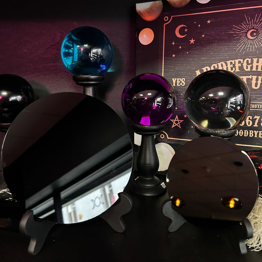 A set of mystical crystal ball tarot cards on black stands, featuring a blue orb, a purple orb, a black orb, a circular black mirror, and a wooden card with gold lettering, displayed against a dark background with a card backing.