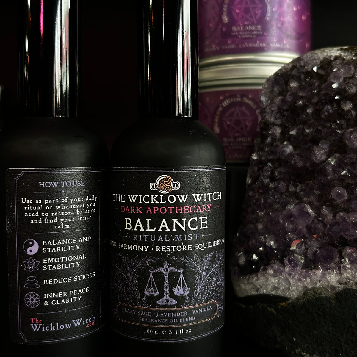 Two black bottles of Wicklow Witch ritual liquids, including 'Balance' and 'Dark Apothecary', displayed alongside a purple amethyst crystal cluster and a purple tin canister on a black background.