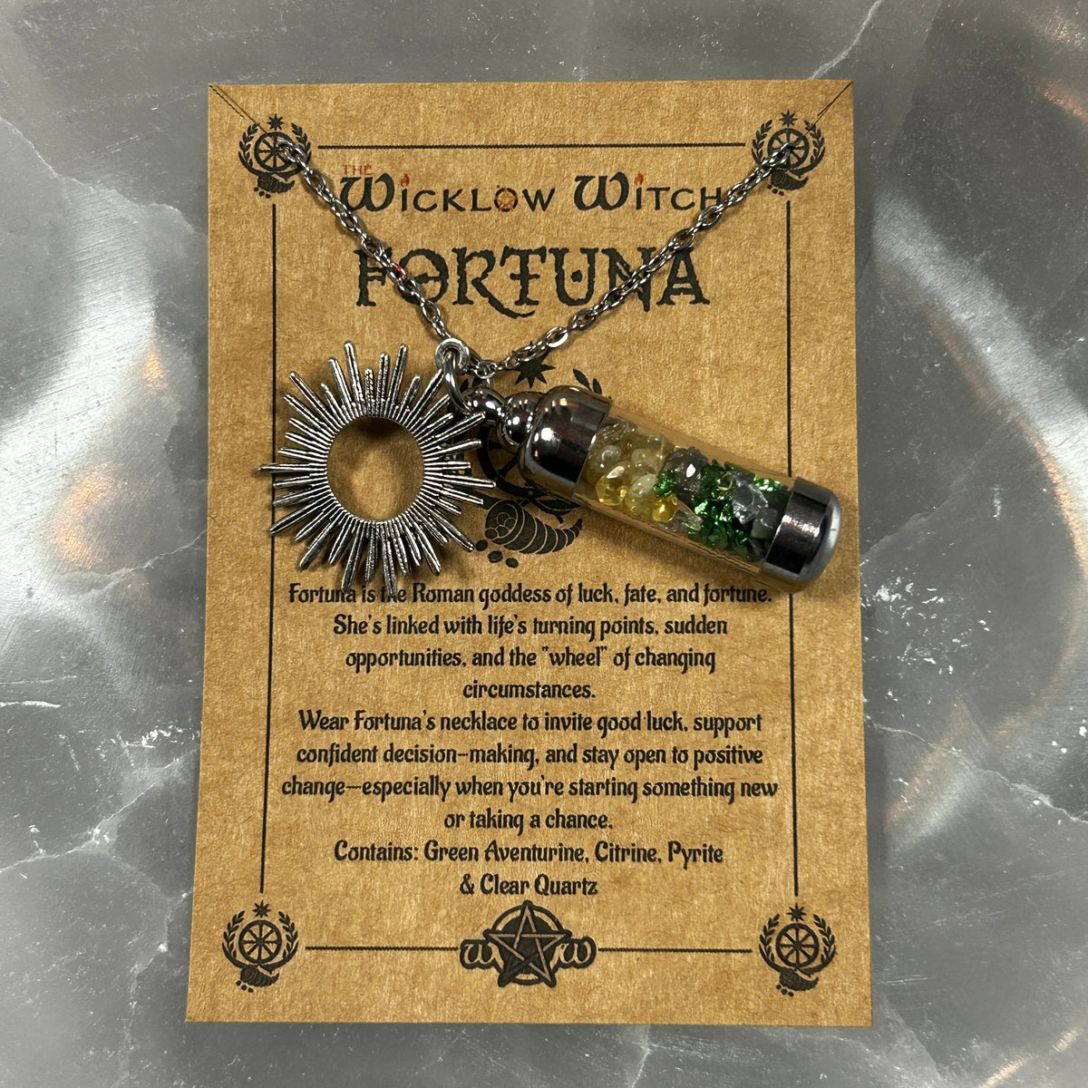 A Wicklow Witch Fortuna pendant necklace displayed on its original tan card. The necklace features a silver-toned sunburst wheel pendant and a clear glass vial filled with green aventurine, citrine, and pyrite, suspended from a silver chain.