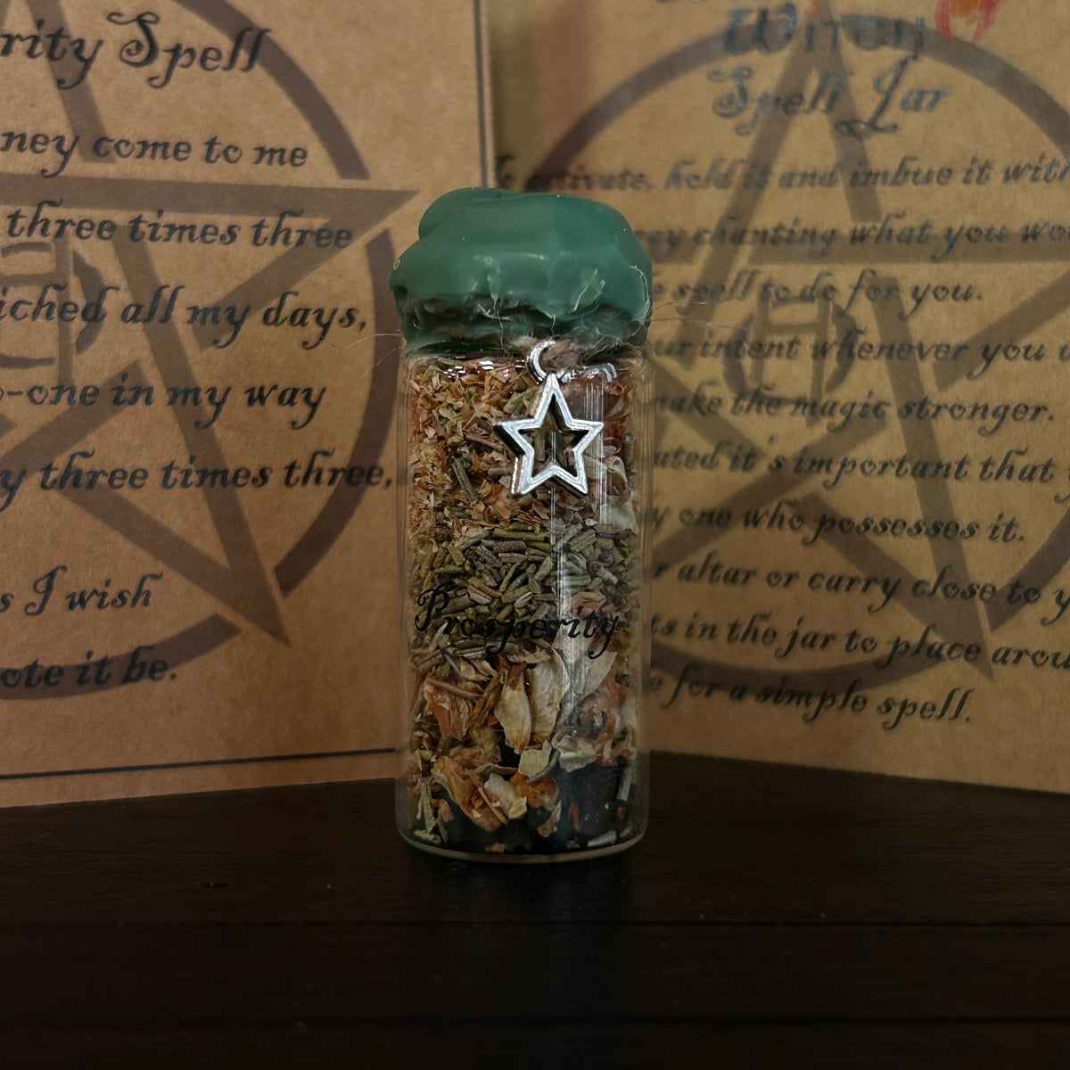 A clear glass jar filled with dried herbs and crystals, topped with a dark green wax seal and decorated with a silver star charm, set against a background of brown parchment paper with occult text.