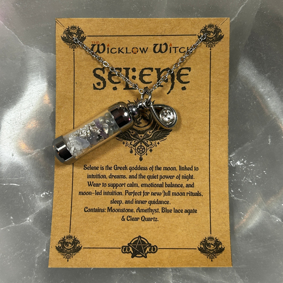 A Selene necklace with a silver amethyst and blue lace agate pendant on a chain, displayed on a brown kraft card labeled 'The Wicklow Witch Selene'.